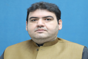 Ein Mann in einer braunen Weste und schwarzem Hemd steht vor einem blauen Hintergrund und scheint über seine lebenslange Haftstrafe nachzudenken.