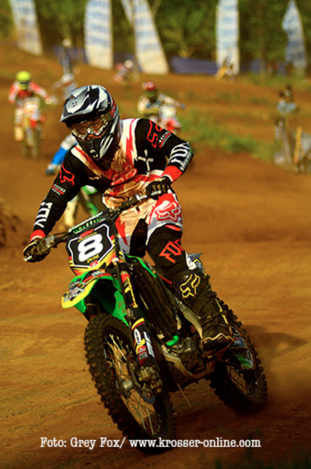 Mehrere Personen bei einem Motorradrennen, alle tragen Helme, mit Text am unteren Bildrand.