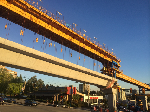 Eine Baustelle in der Innenstadt mit Fahrzeugen und Gebäuden links, unter einem blauen Himmel.