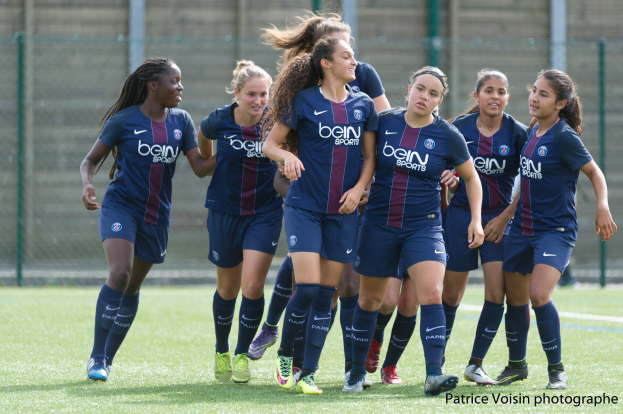 Gruppe junger Frauen beim Fußballspielen auf einem Rasenfeld mit Maschendrahtzaun und einer Wand im Hintergrund, Text "Paris Saint-Germain Women's Soccer" unten rechts.