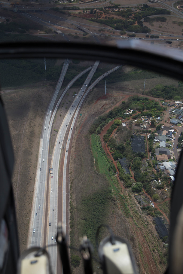 Ein Blick aus dem Inneren eines Flugzeugs, das Fahrzeuge auf Straßen, Bäume, Pfosten und Gebäude durch das Fenster des Flugzeugs zeigt.