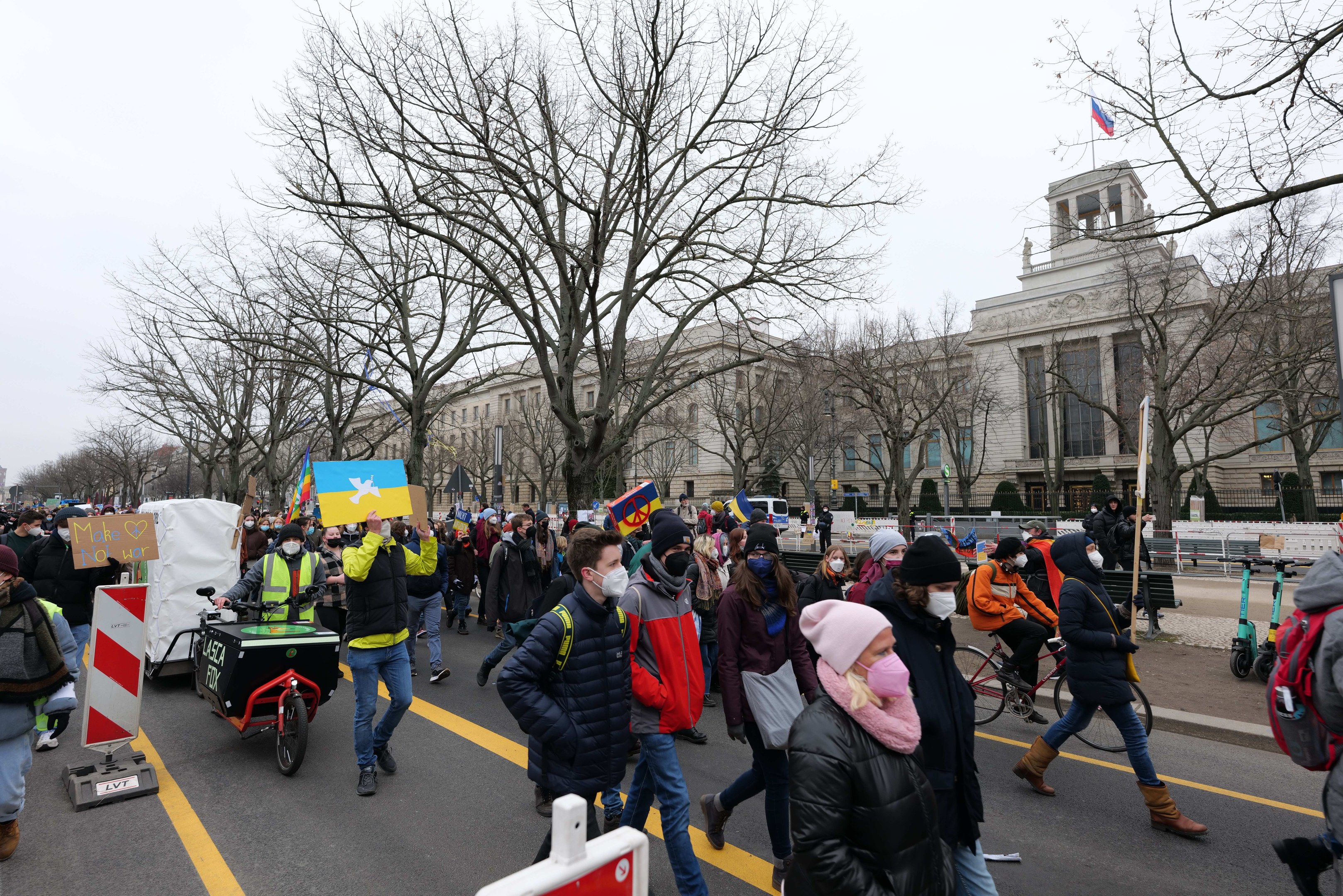 Eine große Gruppe von Menschen nimmt an einer Protestdemo in Washington, D.C. am 21. Januar 2020 teil und marschiert eine Straße entlang, wobei einige Schilder und Banner halten und andere Fahrräder fahren, mit Bäumen, Schildern und einem klaren blauen Himmel im Hintergrund.
