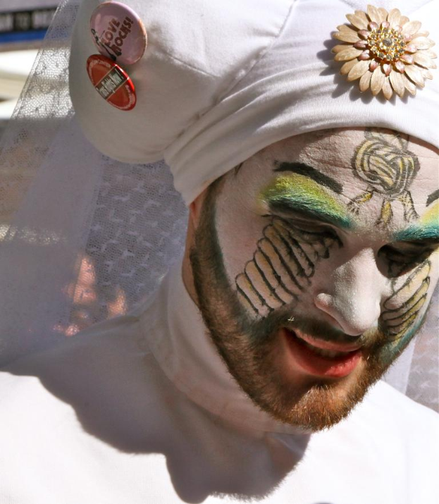 Ein Mann mit Gesichtsbemalung und einer Mütze mit Text, der vor einem Tuchhintergrund steht.