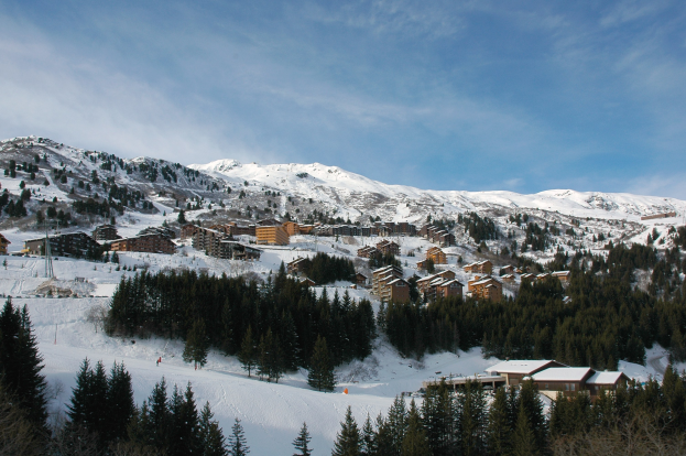Ein Skigebiet in den französischen Alpen mit schneebedeckten Bergen, Bäumen, Gebäuden und einem klaren blauen Himmel.