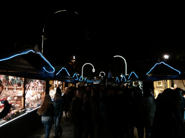 Eine Menschenmenge, die nachts eine Straße entlanggeht und an beleuchteten Ständen vorbeikommt, die verschiedene Artikel auf beiden Seiten der Straße verkaufen.