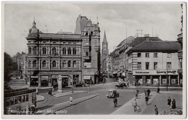 Altes Schwarz-Weiß-Foto einer belebten Münchner Stadtstraße mit Passanten, Fahrzeugen und Gebäuden, Bäumen im Hintergrund und Text unten.