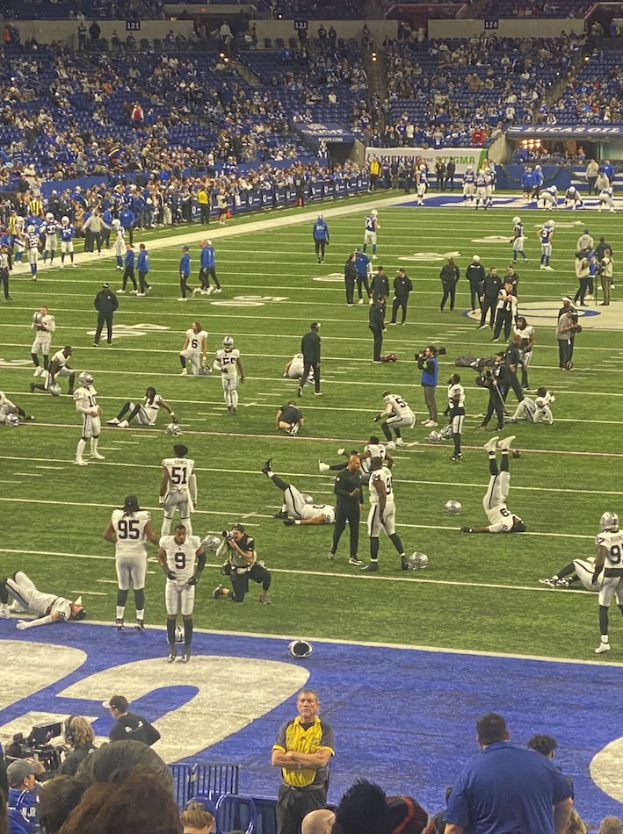 Ein Fußballspiel in einem Stadion mit Menschen auf dem Feld und einigen im Hintergrund sitzend, mit einer Person, die eine Kamera hält, was eine Live-Übertragung anzeigt.