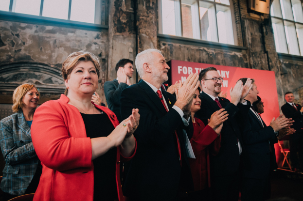 Eine Gruppe von Menschen, die vor einer Menge jubeln und ein Banner mit der Aufschrift "Wahlsieg" hinter sich haben.