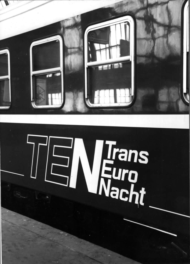Schwarzes und weißes Foto eines Zuges mit der Aufschrift "Trans Euro Nacht" und Fenstern sowie einem Bahnsteig unten.