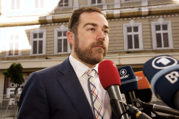 Ein Mann im Anzug spricht zu Medien vor einem Gebäude, wahrscheinlich im Zusammenhang mit einer dreijährigen Haftstrafe.