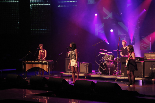 Vier Personen auf einer Bühne mit Musikinstrumenten und Mikrofon.