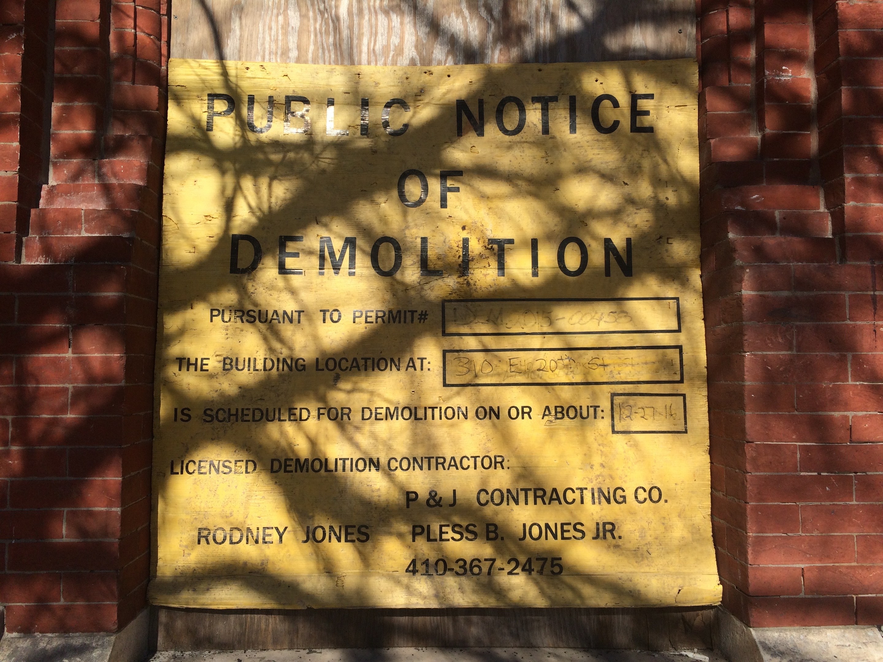 Gelbes Schild auf einem Backsteingebäude mit der Aufschrift "Öffentliche Ankündigung der Abriss" an der Wand angebracht.