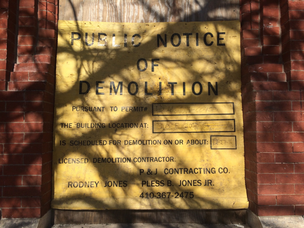 Gelbes Schild auf einem Backsteingebäude mit der Aufschrift "Öffentliche Ankündigung der Abriss" an der Wand angebracht.