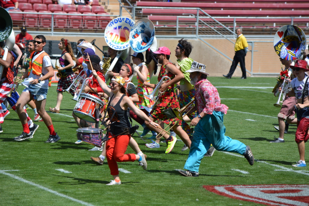 Eine Gruppe von Menschen versammelte sich im Freien mit Trommeln, verschiedenen Instrumenten, Stühlen, Treppen und einem Zaun im Hintergrund.