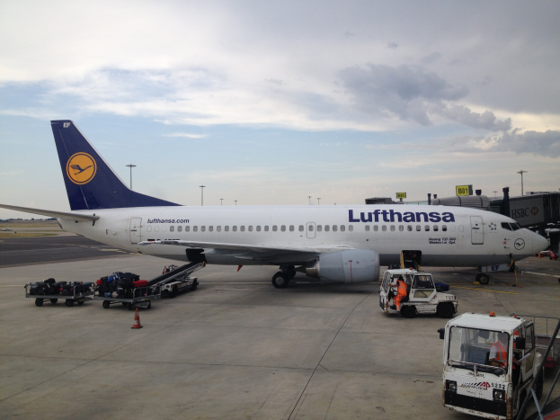 Lufthansa Airbus A320-200 am Frankfurter Flughafen mit Bodenfahrzeugen, Wagen, Verkehrskegeln, Pfählen und Texttafeln vor einem bewölkten Himmel.