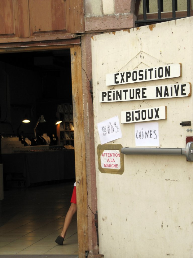 Innenansicht eines Unterschlupfs mit einer Person im Hintergrund neben Treppe und Lampen sowie einer Tür auf der rechten Seite mit Brettern und Text.