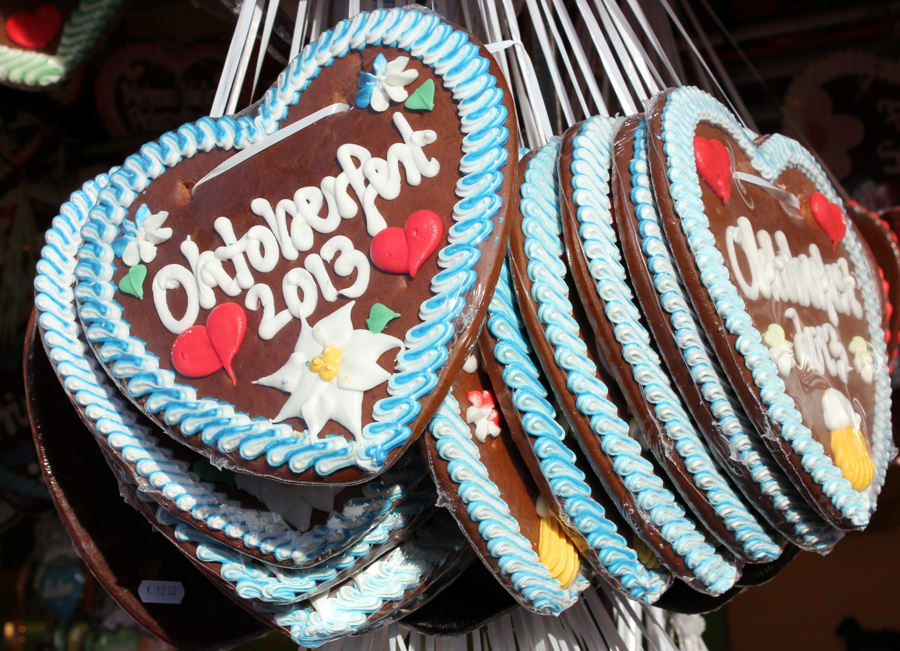 Eine Schnur mit herzförmigen Lebkuchen, die mit buntem Zuckerguss und Streuseln verziert und mit 'Oktoberfest 2013' beschriftet sind, vor einem unscharfen festlichen Hintergrund.