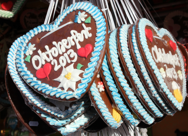 Eine Schnur mit herzförmigen Lebkuchen, die mit buntem Zuckerguss und Streuseln verziert und mit 'Oktoberfest 2013' beschriftet sind, vor einem unscharfen festlichen Hintergrund.