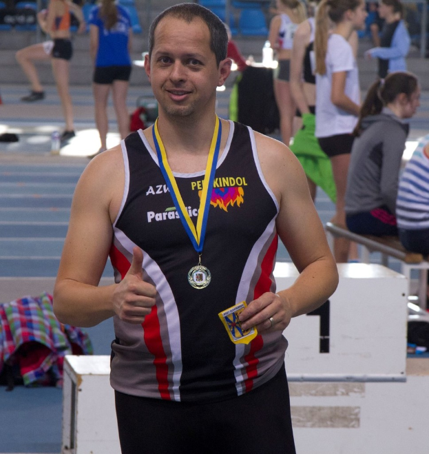 Ein Mann in einem schwarzen Jersey und einer Medaille steht vor einer Gruppe von Menschen, die trainieren.