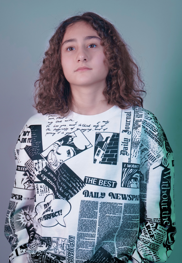 Ein junges Mädchen mit lockigen Haaren, das ein weißes T-Shirt trägt, auf dem steht "Die beste Tageszeitung."