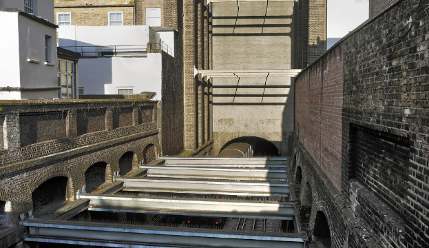 Ein Zug verlässt einen Tunnel zwischen Gebäuden.