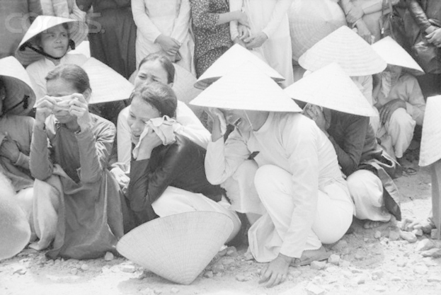 Ein Schwarz-Weiß-Bild von mehreren Menschen, die auf dem Boden sitzen und weinen, mit Steinen unten.