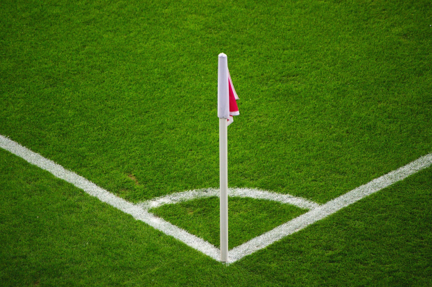 Ein Fuballfeld mit grünem Gras und weißen Begrenzungslinien, das eine weiße Stange mit einer roten und weißen Flagge zeigt, die den Elfmeterpunkt markiert.