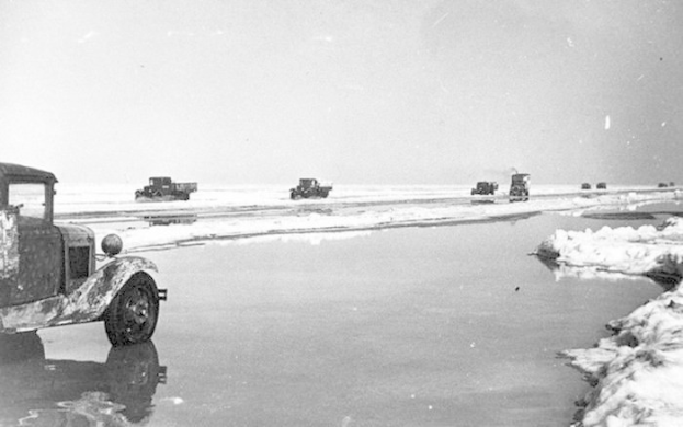Eine Gruppe von Lastwagen fährt auf einer schneebedeckten, gefrorenen Straße mit einem klaren Himmel im Hintergrund.