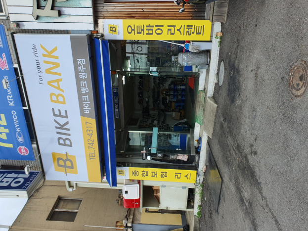 Ein Fahrradgeschäft namens "Bike Bank" mit Fahrzeugen davor geparkt, einer Straße auf der rechten Seite und verschiedenen Gegenständen und Texttafeln im Inneren.