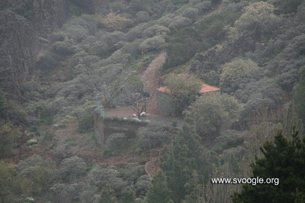 Ein Gebäude auf einem Berg umgeben von Bäumen mit Text in der rechten unteren Ecke.
