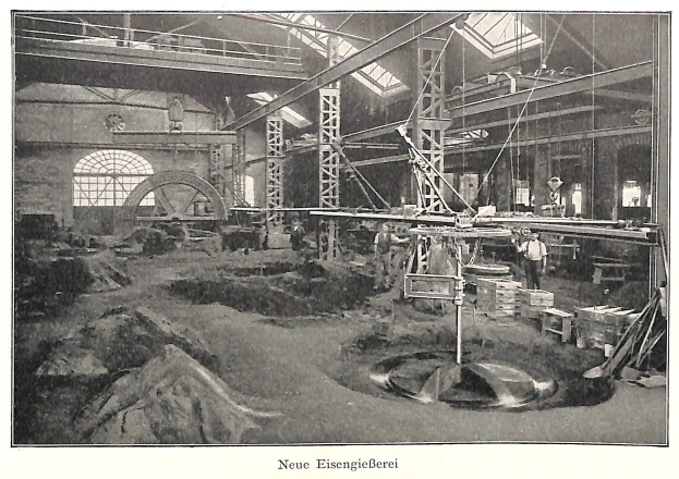 Schwarzes und weißes Foto einer Fabrik mit Arbeitern, die Maschinen bedienen, umgeben von Metallstangen und -pfählen, beschriftet mit "Neue Eisenglebeerei, die erste Fabrik Deutschlands" unten.