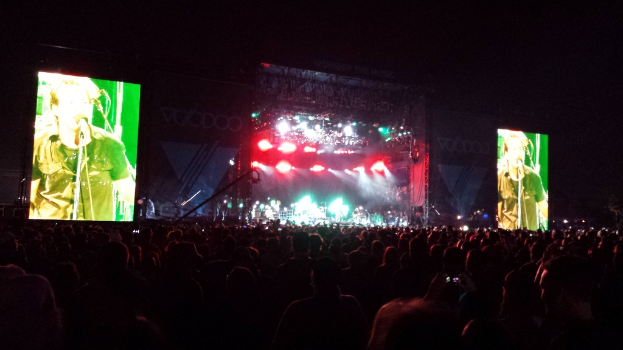 Eine Konzertszene mit einer Menge unten und großen Bildschirmen links und rechts.