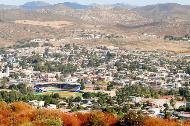 Eine Landschaft mit Häusern, Bäumen, Strommasten, Hügeln und einem klaren Himmel.