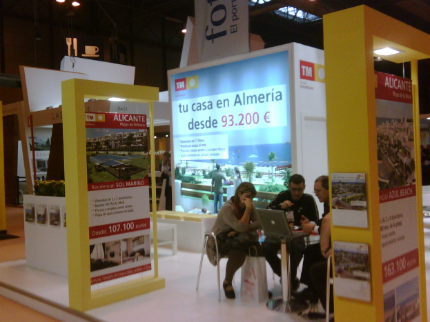 Eine Gruppe von Menschen, die um einen Tisch herum auf Stühlen sitzen und auf einen Laptop schauen, mit mehreren Flyern, auf denen verschiedene Werbeanzeigen zu sehen sind.