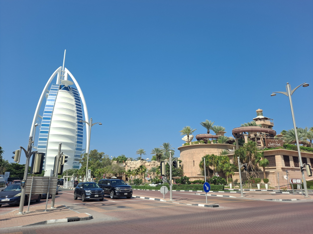 Das Burj Al Arab Hotel in Dubai, VAE, mit umliegenden städtischen Elementen wie Fahrzeugen, Verkehrszeichen, Werbetafeln, Pflanzen, Bäumen und Gebäuden unter einem sichtbaren Himmel.