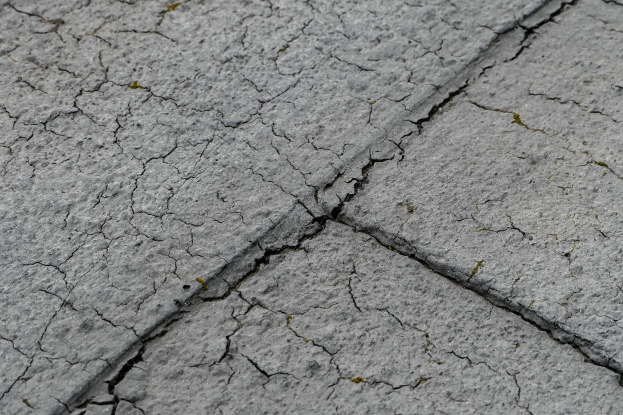 Nahaufnahme einer gebrochenen und unebenen Straßoberfläche mit tiefen, breiten Rissen.