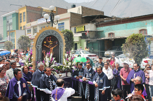 Menschen auf einer Straße mit einem Kreuz und Blumenbouquets in der Mitte, Autos im Hintergrund und Gebäude, Bäume und Straßenlaternen