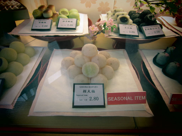 Verschiedene Lebensmittel auf einem Blatt Papier mit Preiszetteln, umgeben von anderen Gegenständen.