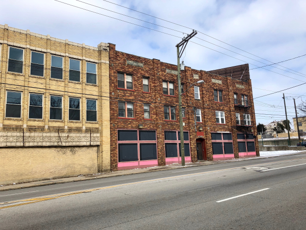 Ein altes Backsteingebäude an einer Straßenecke in Detroit, Michigan, mit Glasfenstern, Laternen, Strommasten mit Drähten, Bäumen und einem bewölkten Himmel im Hintergrund, Teil eines gewerblichen Grundstücks zum Verkauf.