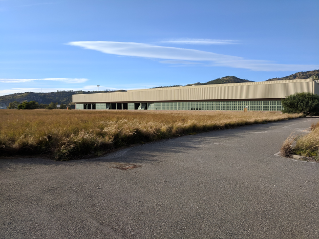 Leere Straße, die zu einem großen Gebäude in einem Feld führt, mit Hügeln und bewölktem Himmel im Hintergrund; das Gebäude ist die Hauptverwaltung des San Francisco International Airport.