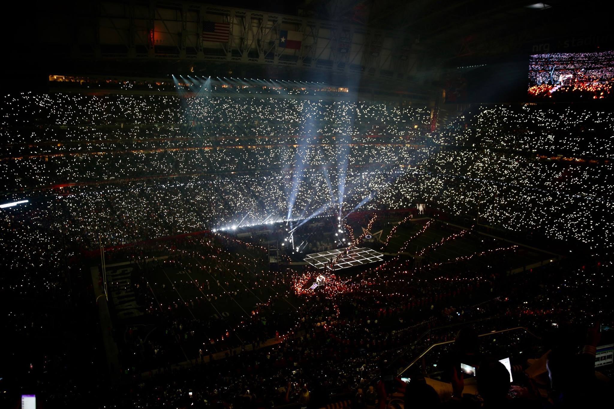 Eine große Menschenmenge in einem hell erleuchteten Stadion bei Nacht schaut auf einen Bildschirm mit den Ergebnissen der Super Bowl XLVII-Halbzeitshow.