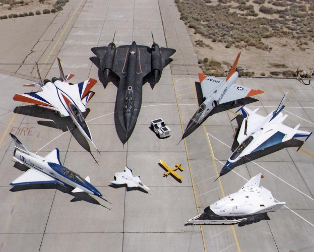 Ein Jetflug ist im Bildzentrum zu sehen, darunter eine Start- und Landebahn sowie Büsche im Hintergrund.