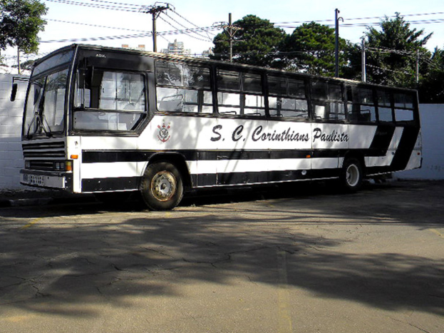 Ein Bus steht auf einer Straße mit einer Wand, Strommasten mit Kabeln, Bäumen, Gebäuden und dem Himmel im Hintergrund.