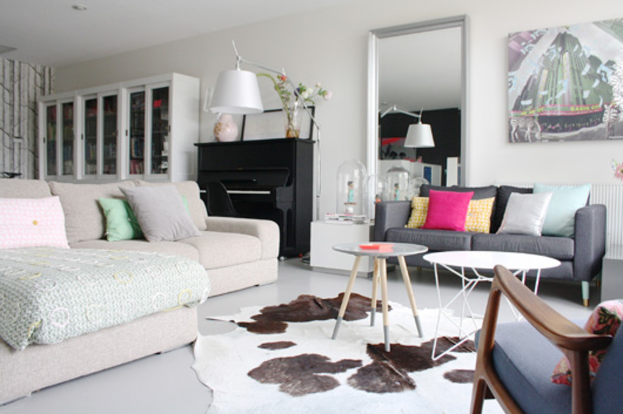 Ein Wohnzimmer mit zwei Sofas, zwei Tischen, einer Lampe, einem Kissen, einem Spiegel, einem Musikinstrument und einer Vitrine an einer Wand.