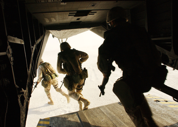 Soldaten in Uniform und Helmen steigen aus einem Flugzeug und halten Gewehre, was auf eine militärische Operation hinweist.
