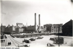 Ein Schwarz-Weiß-Foto einer Stadtstraße mit Gebäuden, Pfählen, Fahrzeugen, Menschen, Bahnschienen und anderen Gegenständen, mit dem Text "GmbH & Co. KG" unten.