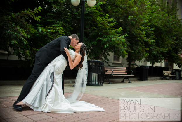 Brautpaar küsst vor Bänken, Mülltonnen und Bäumen