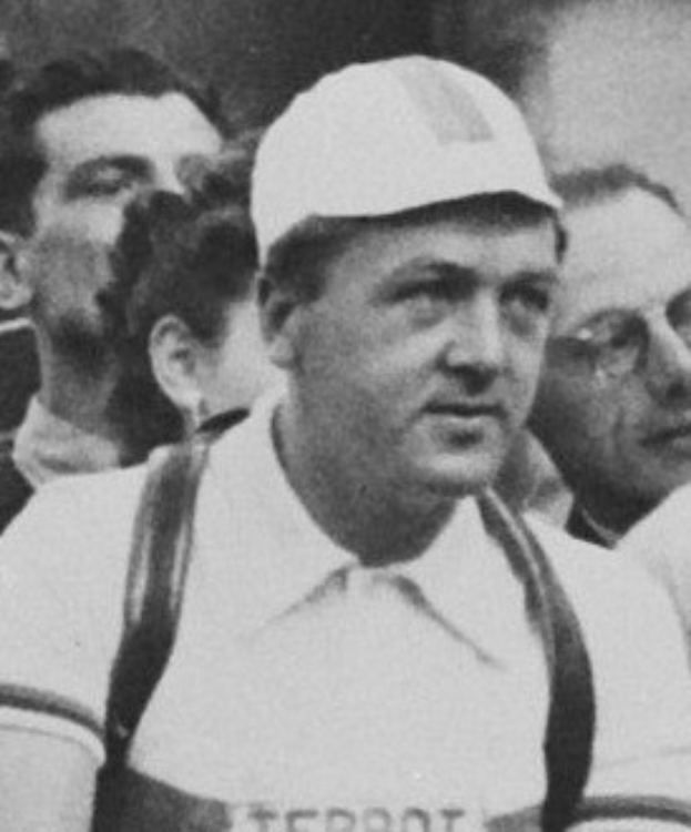 Ein Schwarz-Weiß-Foto eines Mannes in einer Mütze und Hosentägern, der vor einer Gruppe von Menschen steht, der als legendärer Fussballspieler gilt.