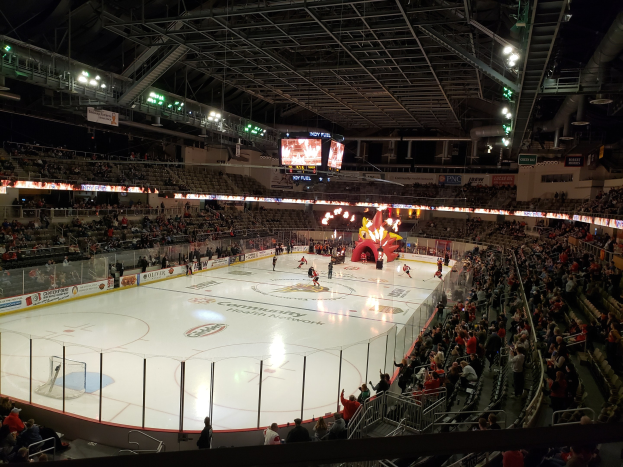 Eishockeyspiel in einer großen Arena mit Zuschauern, Eisfläche von einem Zaun umgeben, Banner, Metallstangen und Lampen oben, zwei Bildschirme und die Columbus Blue Jackets Arena.