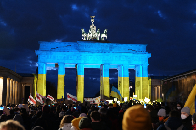 Eine Menschenmenge steht vor dem Brandenburger Tor in Berlin, Deutschland, mit Fahnen und Schildern, mit einem Banner auf der rechten Seite.